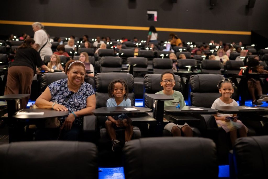 A grandparent and three grandchildren sit in a movie theatre together.