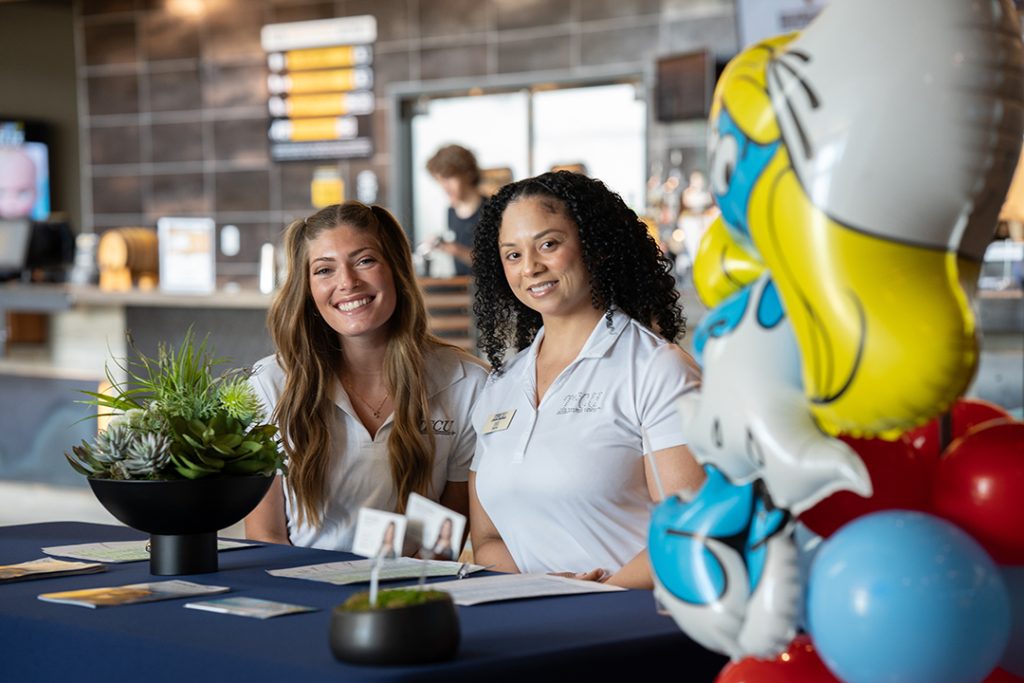 Two women smiling behind a table while registering members for the movie event.