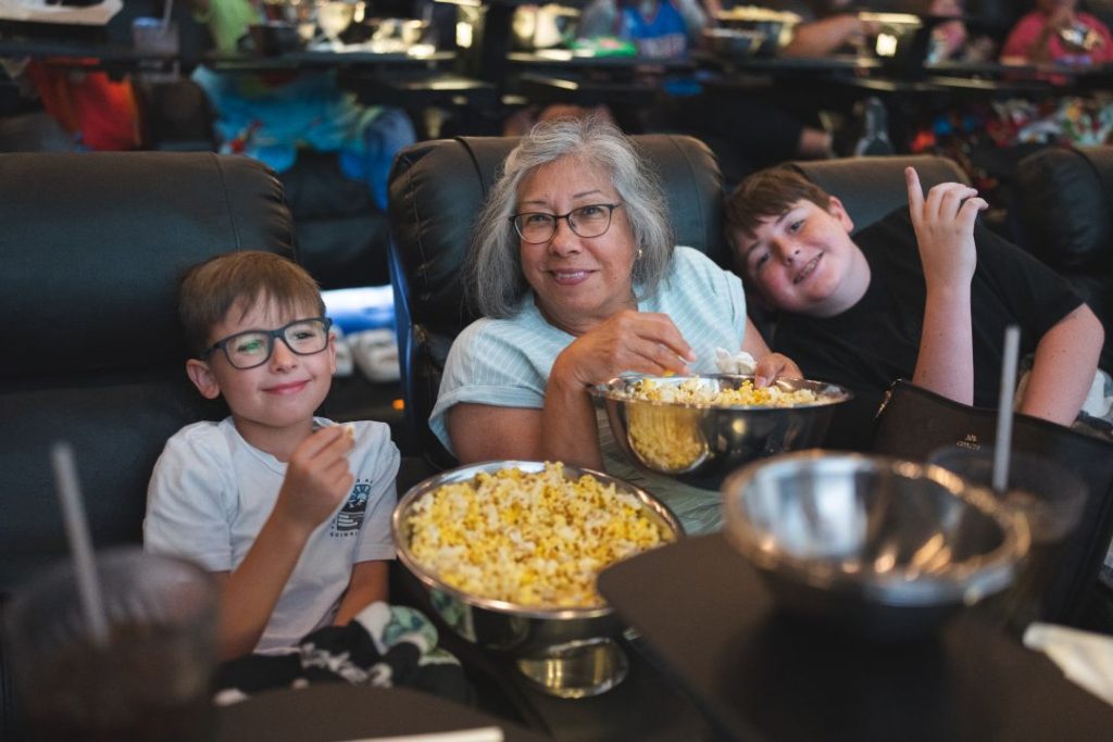 Two children and an adult eat popcorn in a movie theater