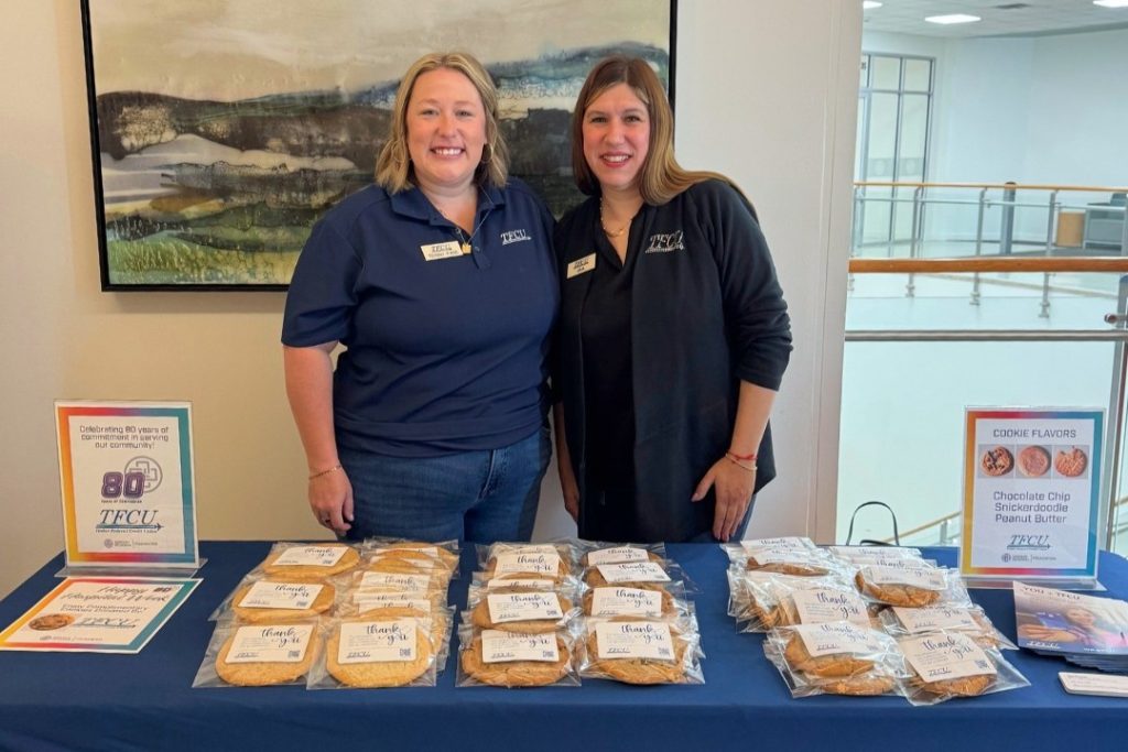 Two TFCU employees stand in front of a table with cookies
