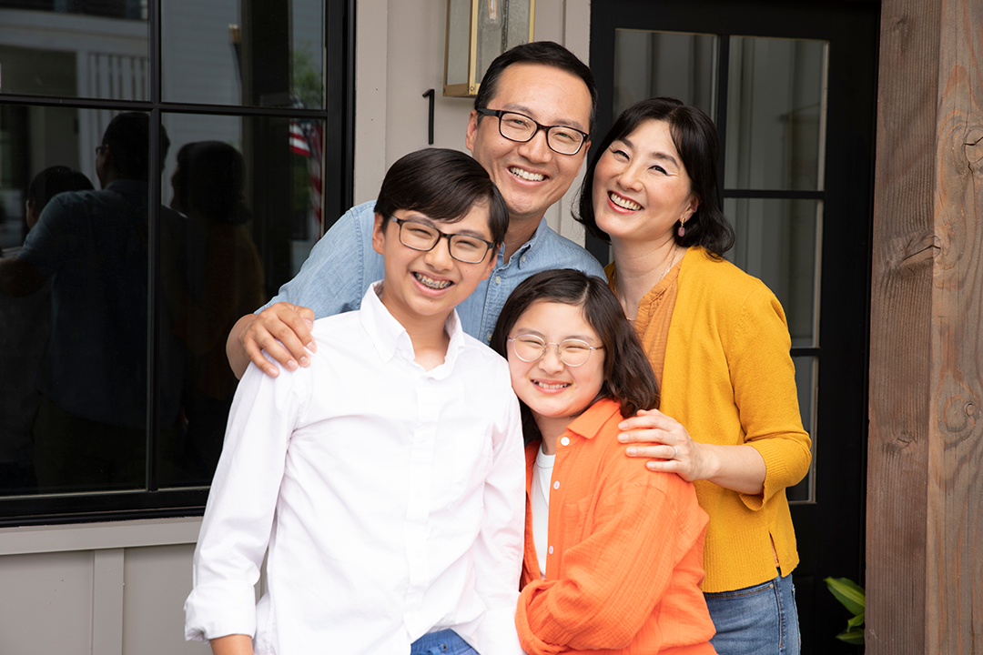 A family of four posing for the camera and standing on a porch.