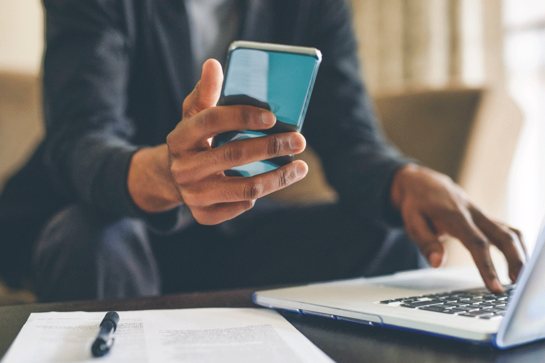 Close up of someone holding their mobile smartphone with their laptop