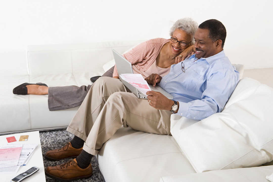 Cheerful senior couple sitting on couch and using laptop