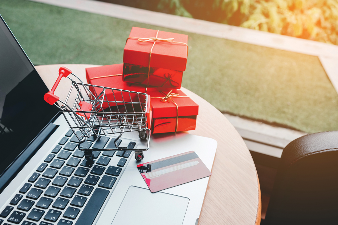 A laptop with credit card, toy shopping cart and three small red wrapped presents to help visualize online shopping.