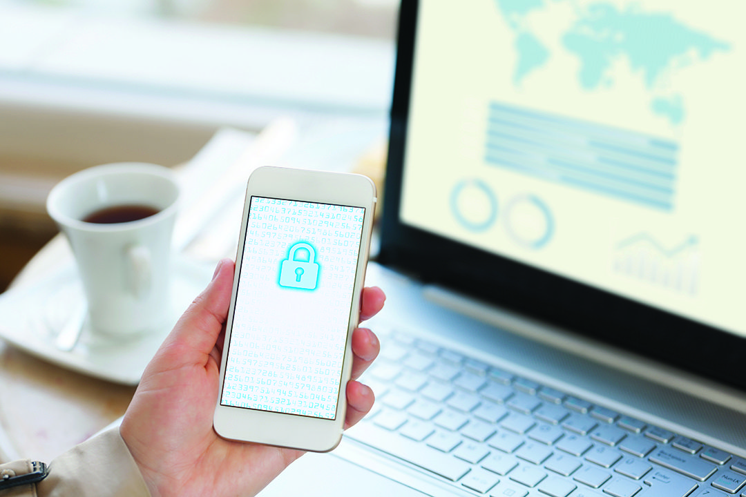 Close up of a smartphone with a lock on the screen and a laptop and coffee cup in the background.