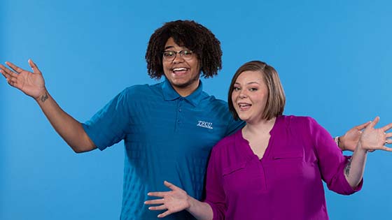 Two employees standing together with their arms up.