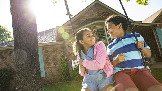 Two young kids on a swing in front of a house