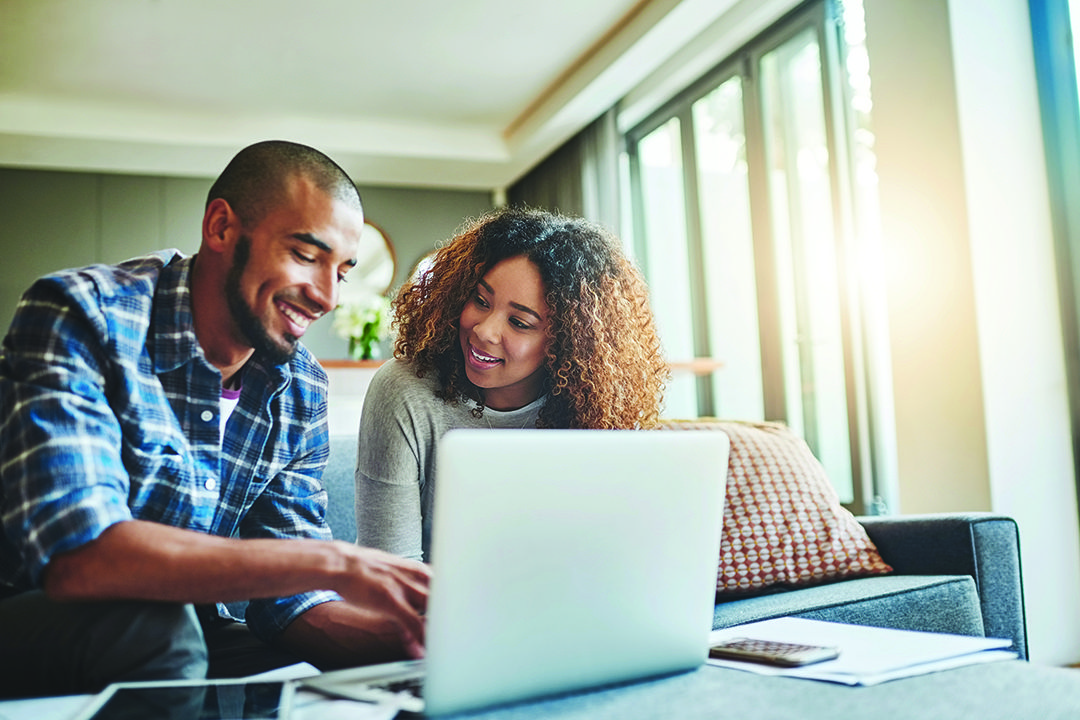 A Young couple using a laptop in their home and smiling.