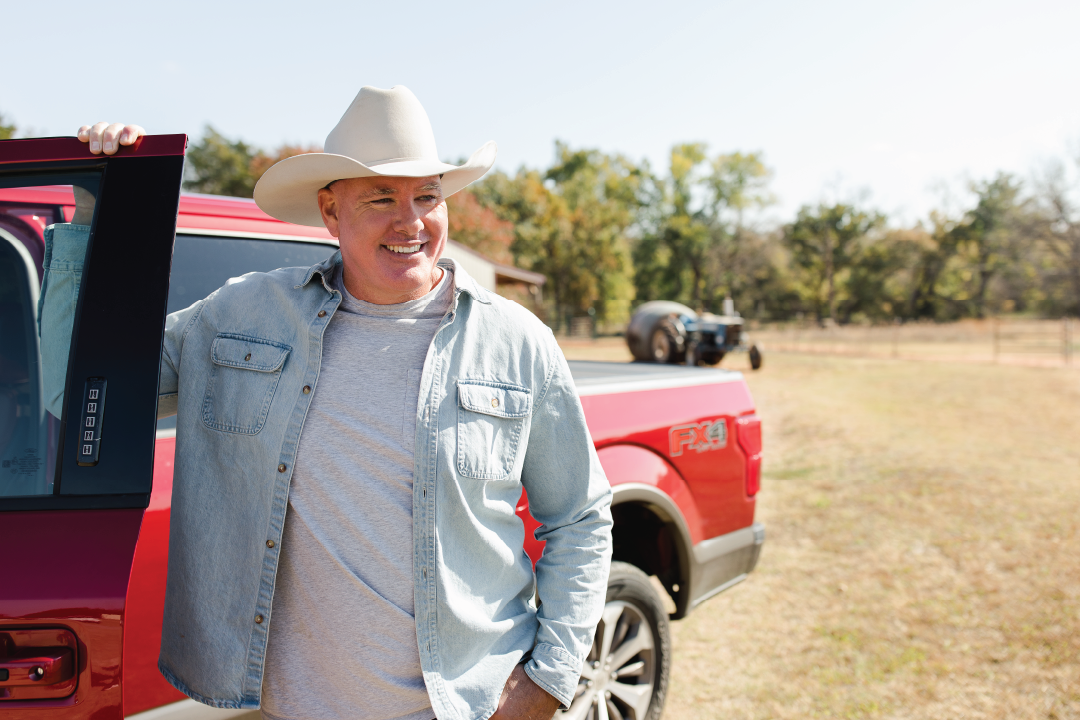 Cowboy man standing by and holding the door of his red truck.