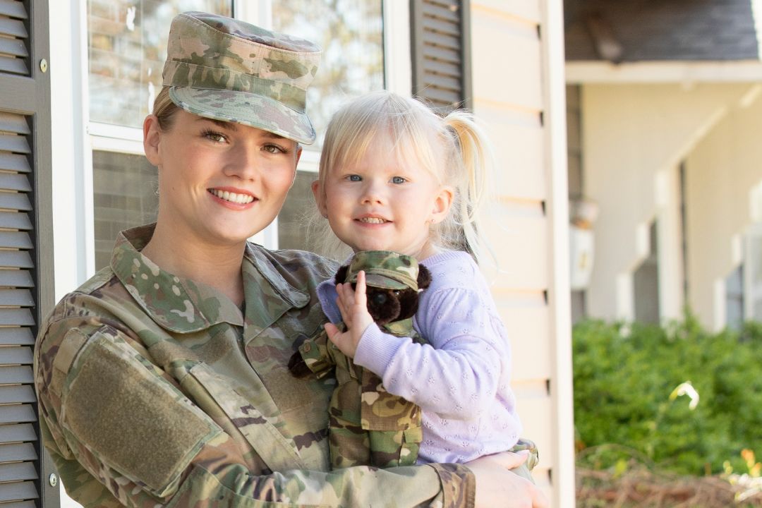 A woman in military uniform holds a young girl outside