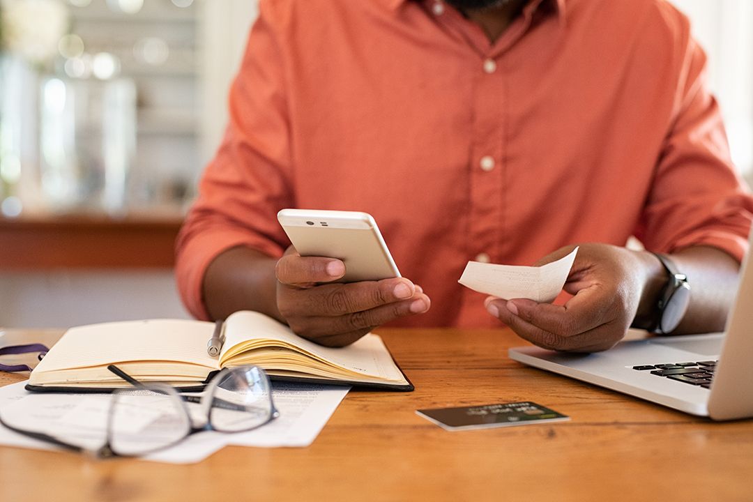 Close up of someone holding a mobile phone and a piece of paper sitting at a table