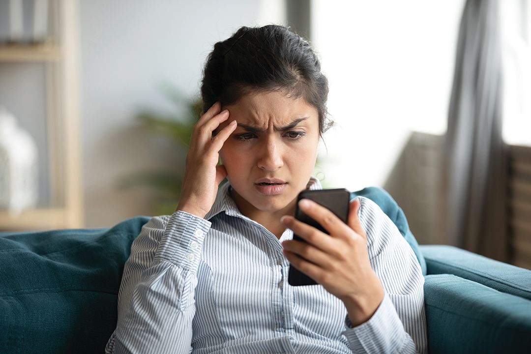 A woman who is looking at her mobile phone and is looking stressed and worried