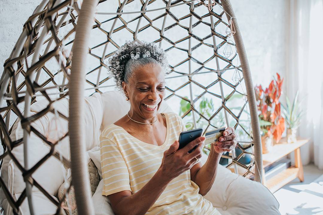 Older woman sitting on a chair, on her phone holding a credit card.
