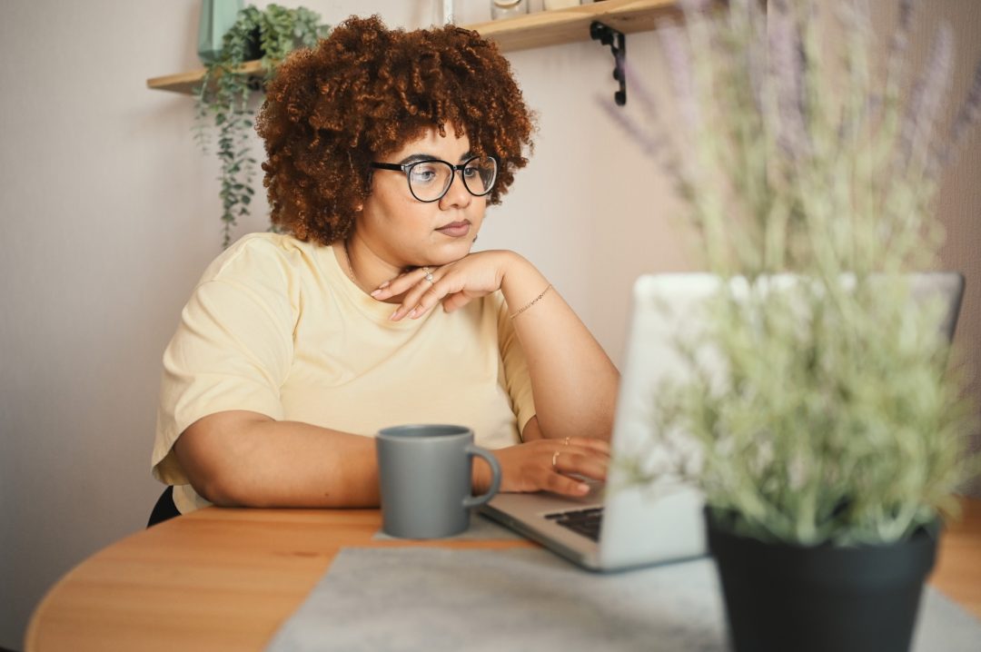 A young woman with glasses scrolls on her laptop.