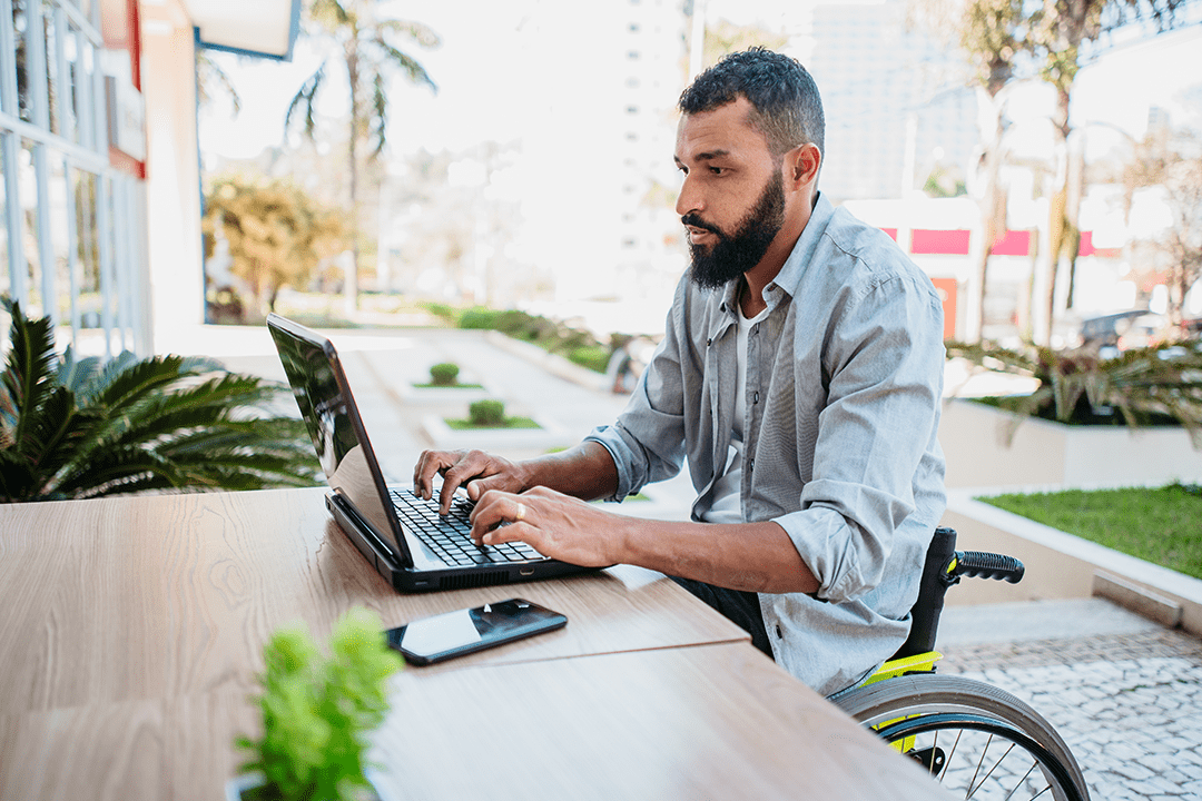 Young man in wheelchair outside on his laptop