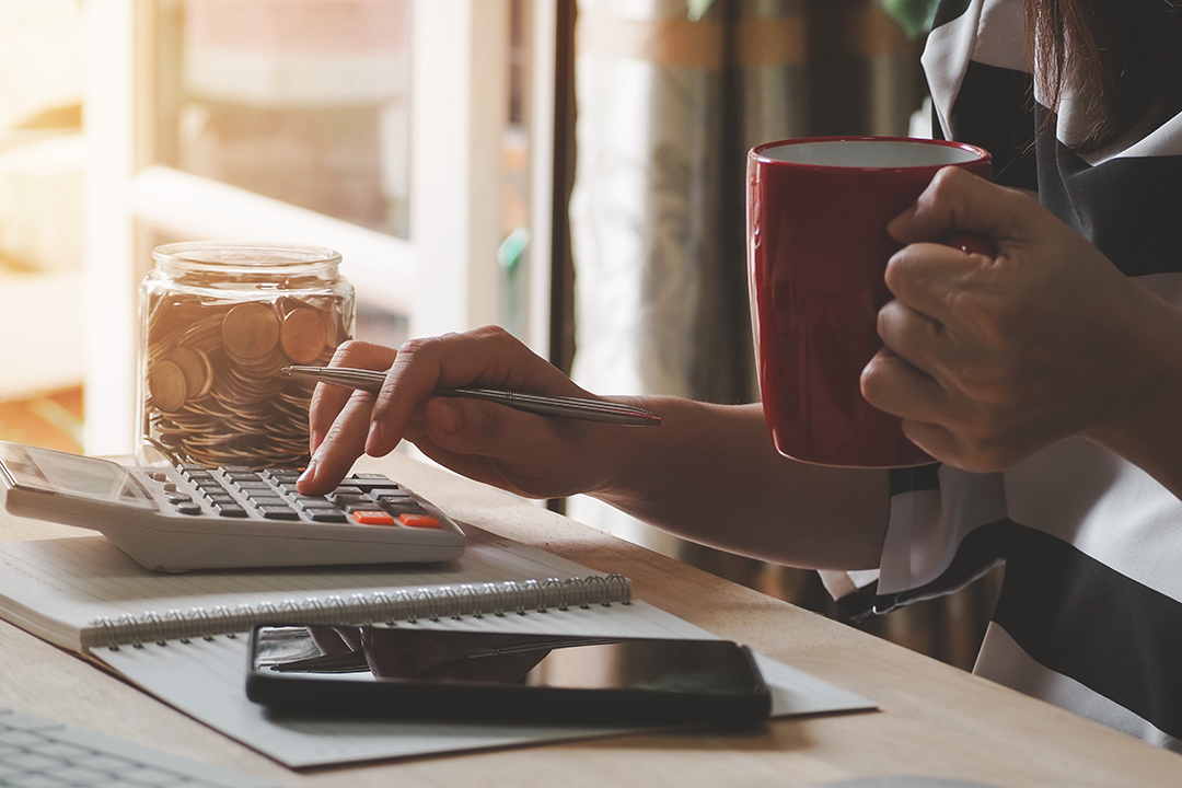 Close up of someone holding a red mug and pen while typing on a calculator.