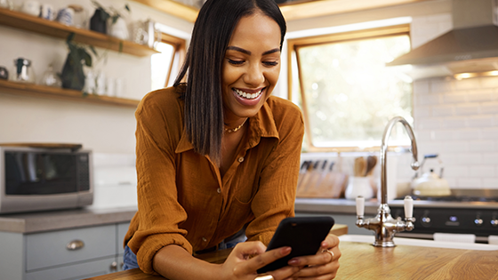 A woman in the kitchen leaning over the counter while on her phone.