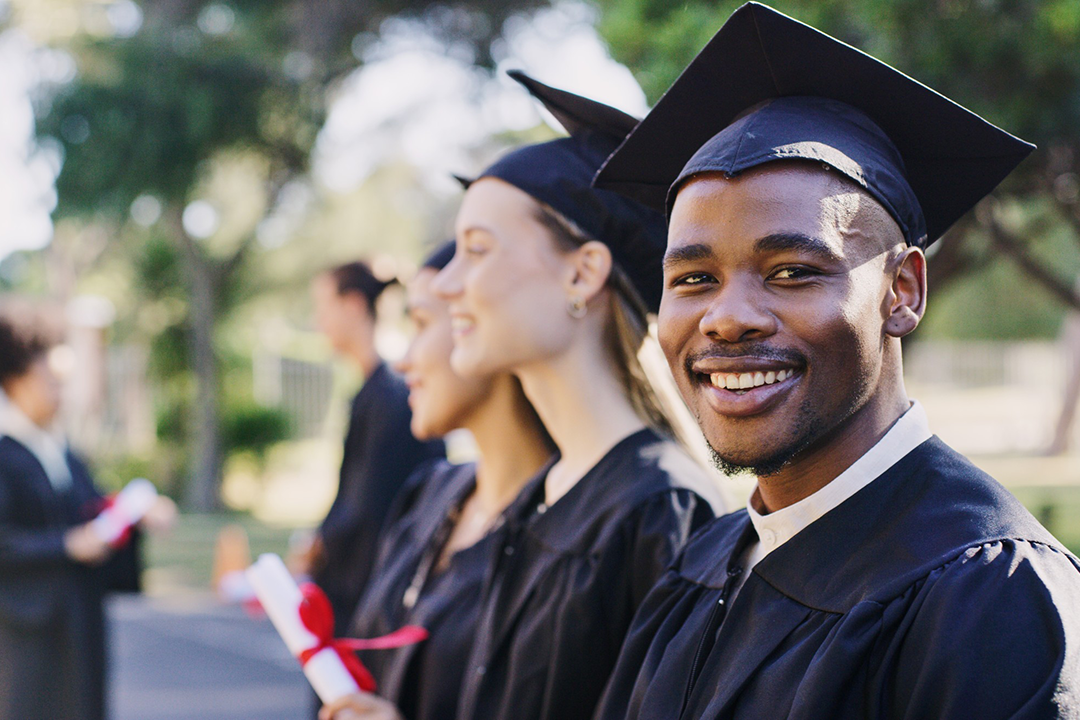 College graduates standing in a row with one of them looking at the camera