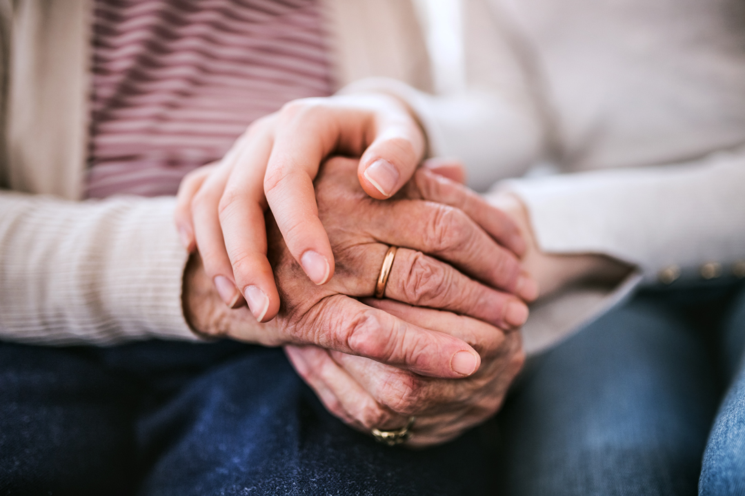 Close-up of clasped hands of elderly woman and young woman.