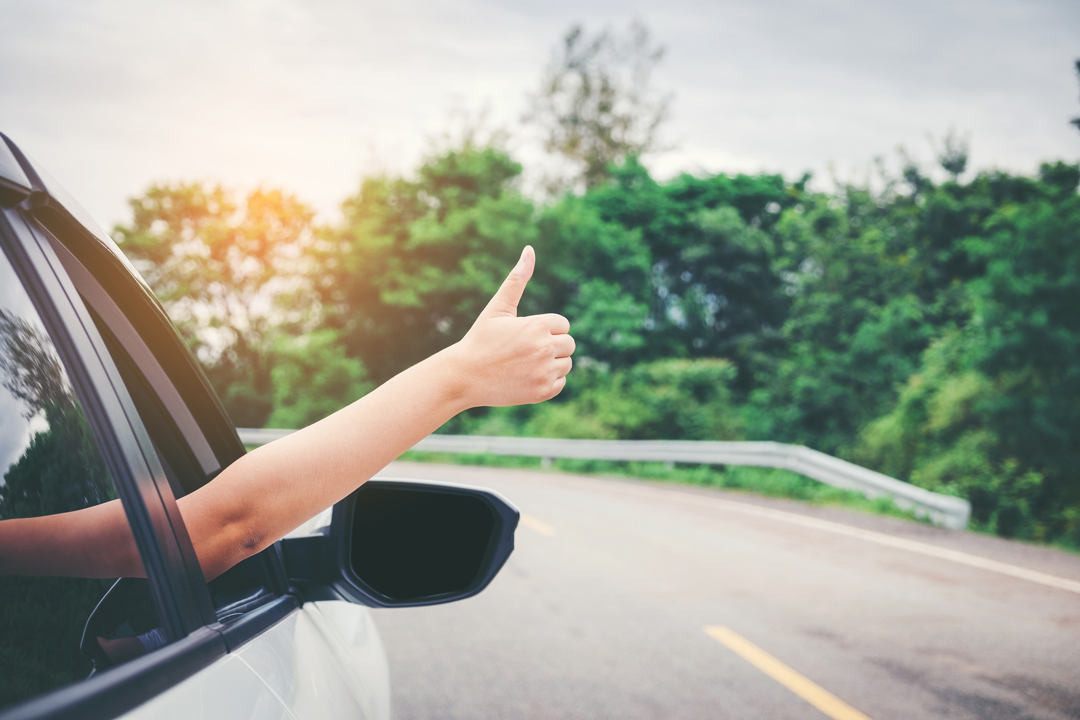 Close up of passenger side of a traveling vehicle with a woman giving a thumbs up signal.