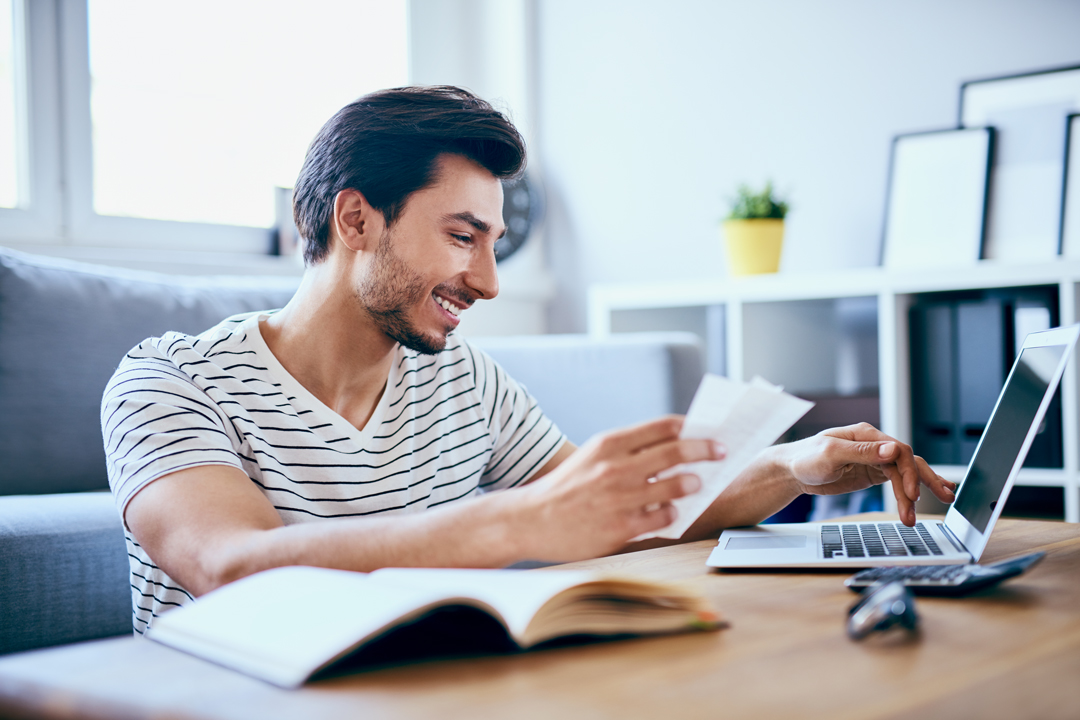 Happy man paying bills on his laptop in living room