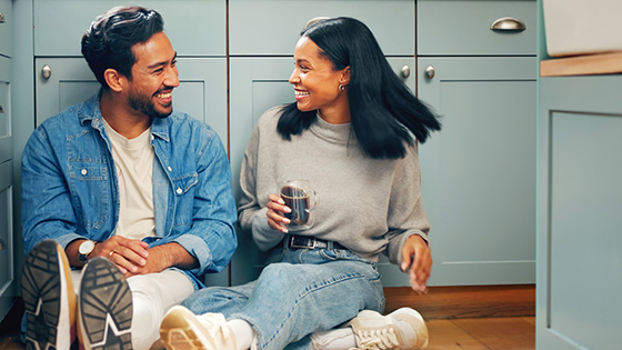 A man and woman sit on the floor of a kitchen