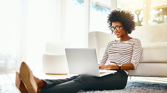 Happy woman sitting on floor working on laptop.