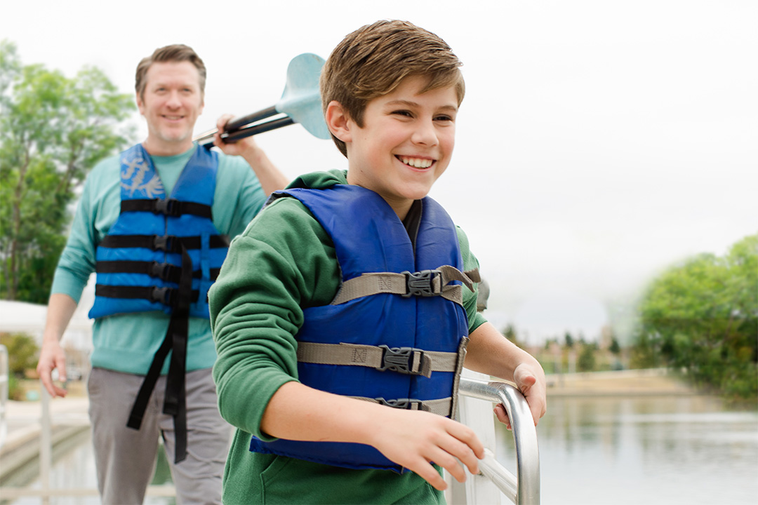 A son with a lifejacket smiling with his dad behind him holding a paddle