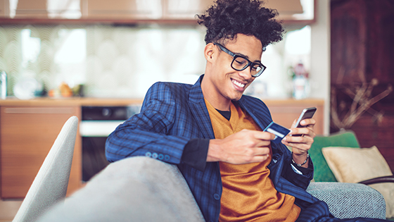 Man sitting on couch, using his TFCU credit card to make an online purchase.