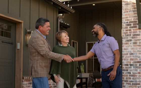 A man smiles and shakes hands with another man and woman