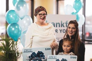 Two women who are TFCU members are each holding a TFCU gift card sign with a little girl sitting in one of the woman's lap.