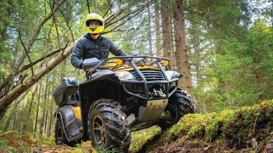 An outdoorsman drives his ATV along a trail in the woods.