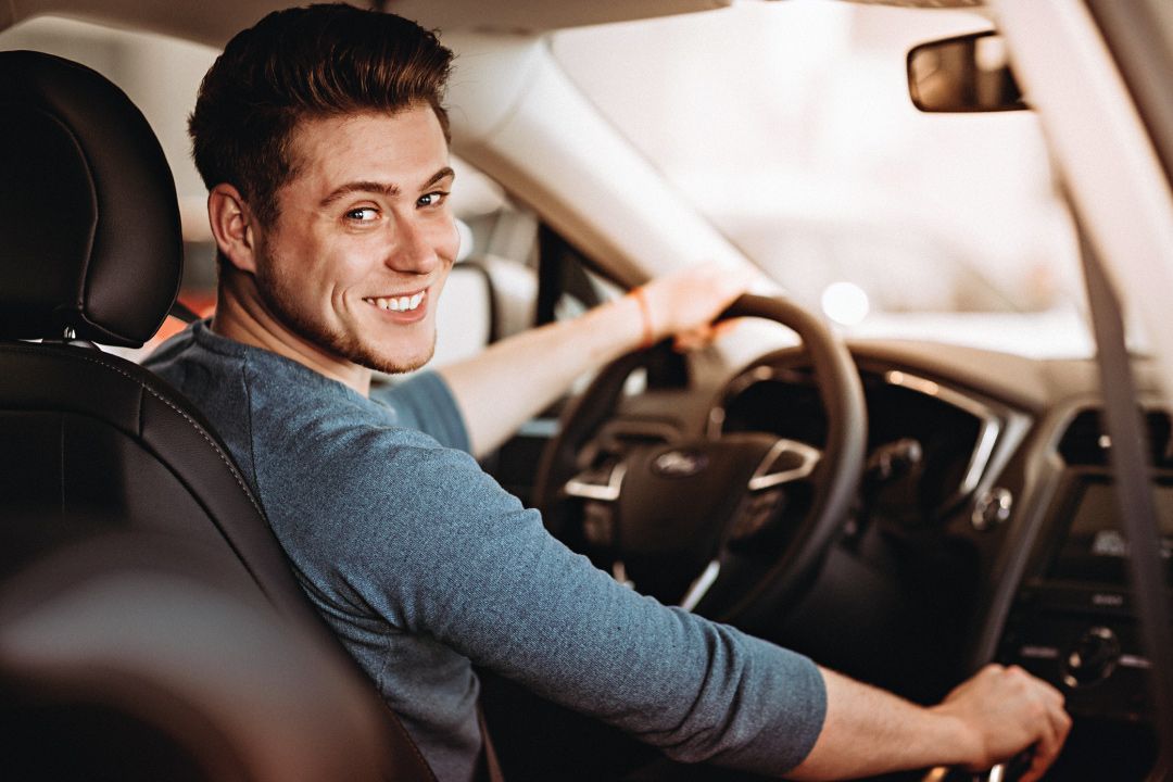 Young first time car buyer sitting in new car and smiling