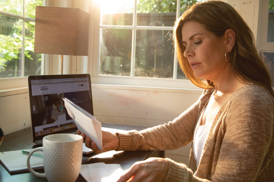 woman at desk with laptop paying bills with checks