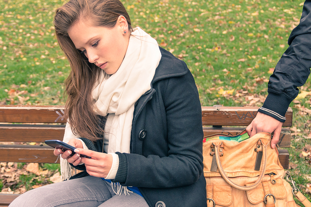 Distracted, young woman on park bench having purse stolen.