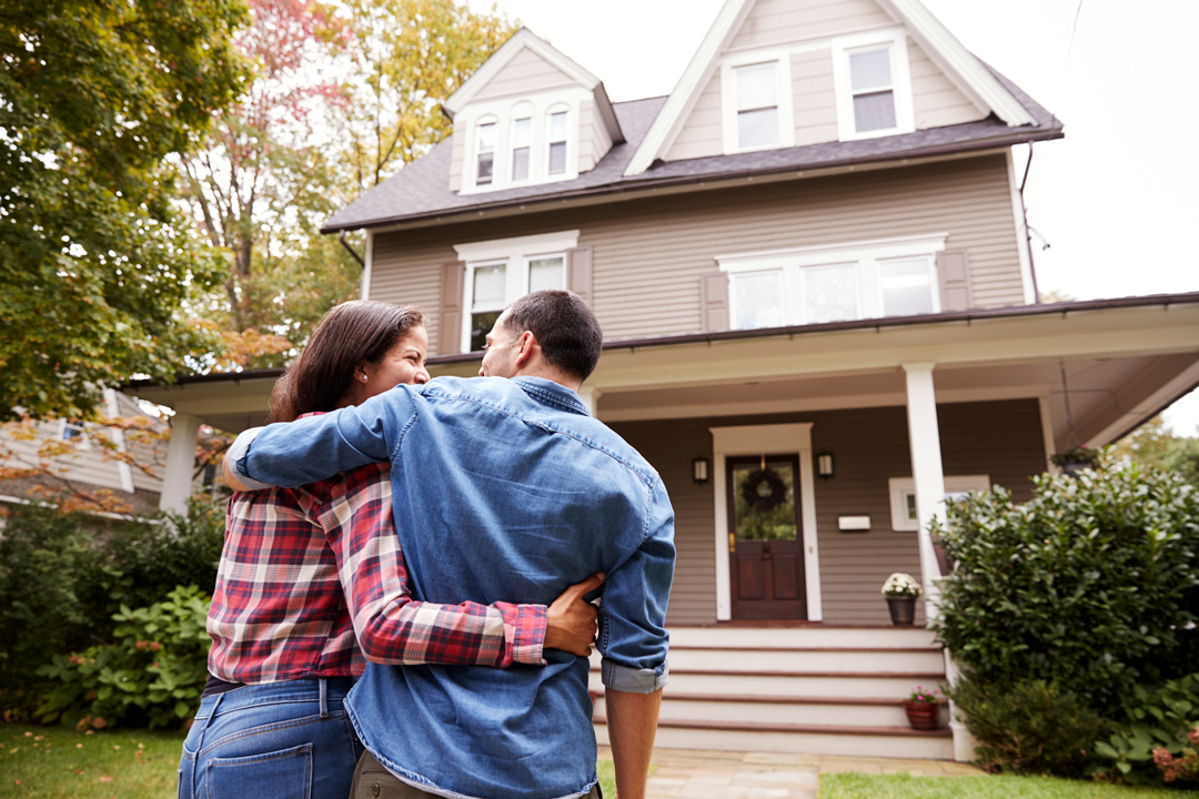 Man and woman walking with their arms lovingly around each other toward a beautiful new two-story home.