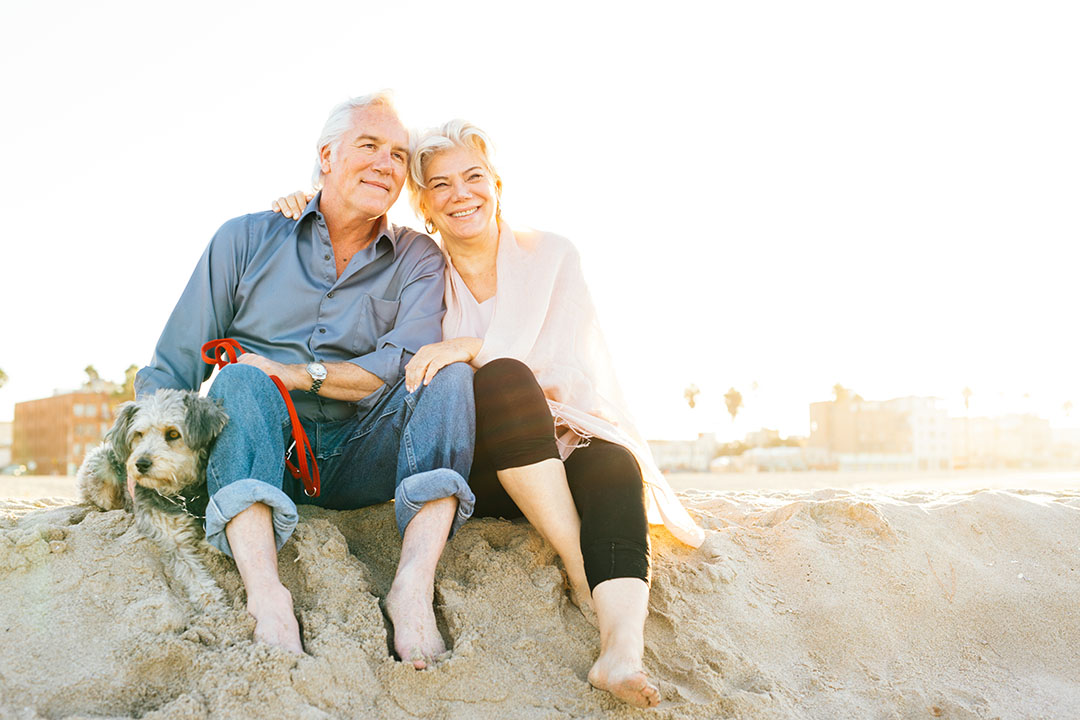 Senior couple sitting on the beach with dog.