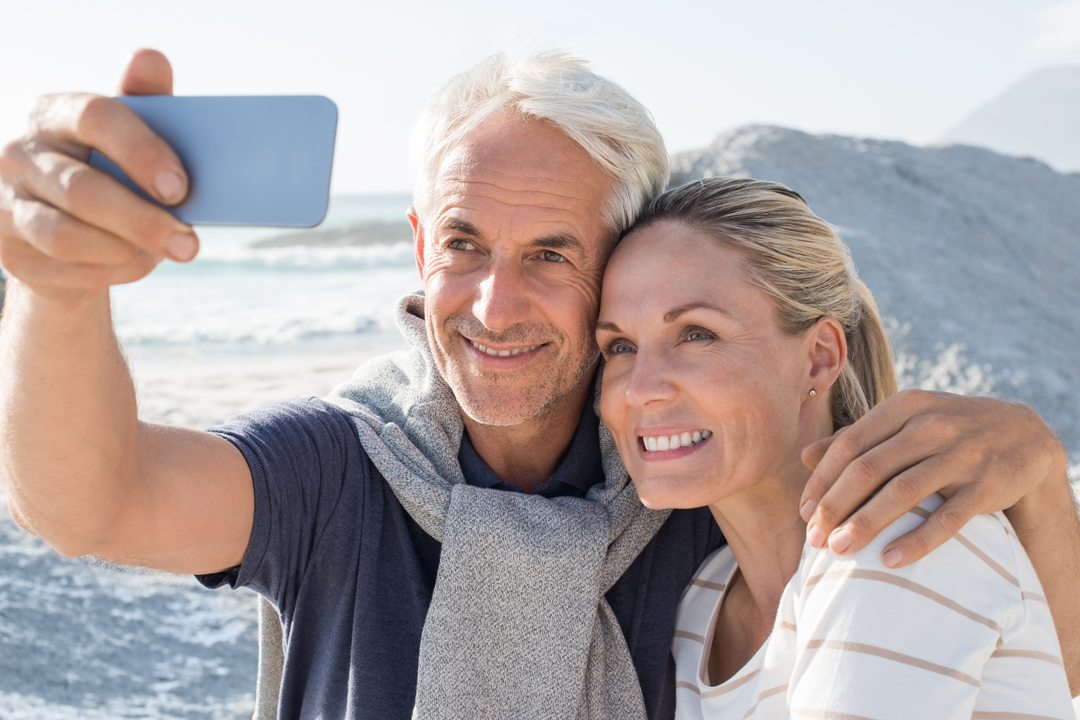 Senior man and woman taking selfie with the ocean behind them.