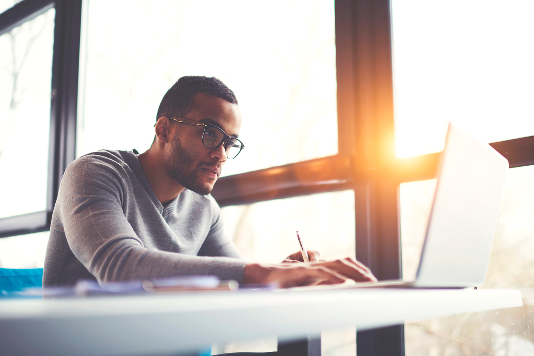 Serious dark skinned young man wearing glasses and searching for information online.