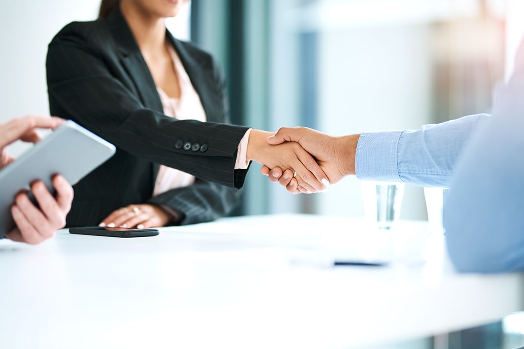 Close up shot of a business woman shaking hand with a businessman in a modern looking office.