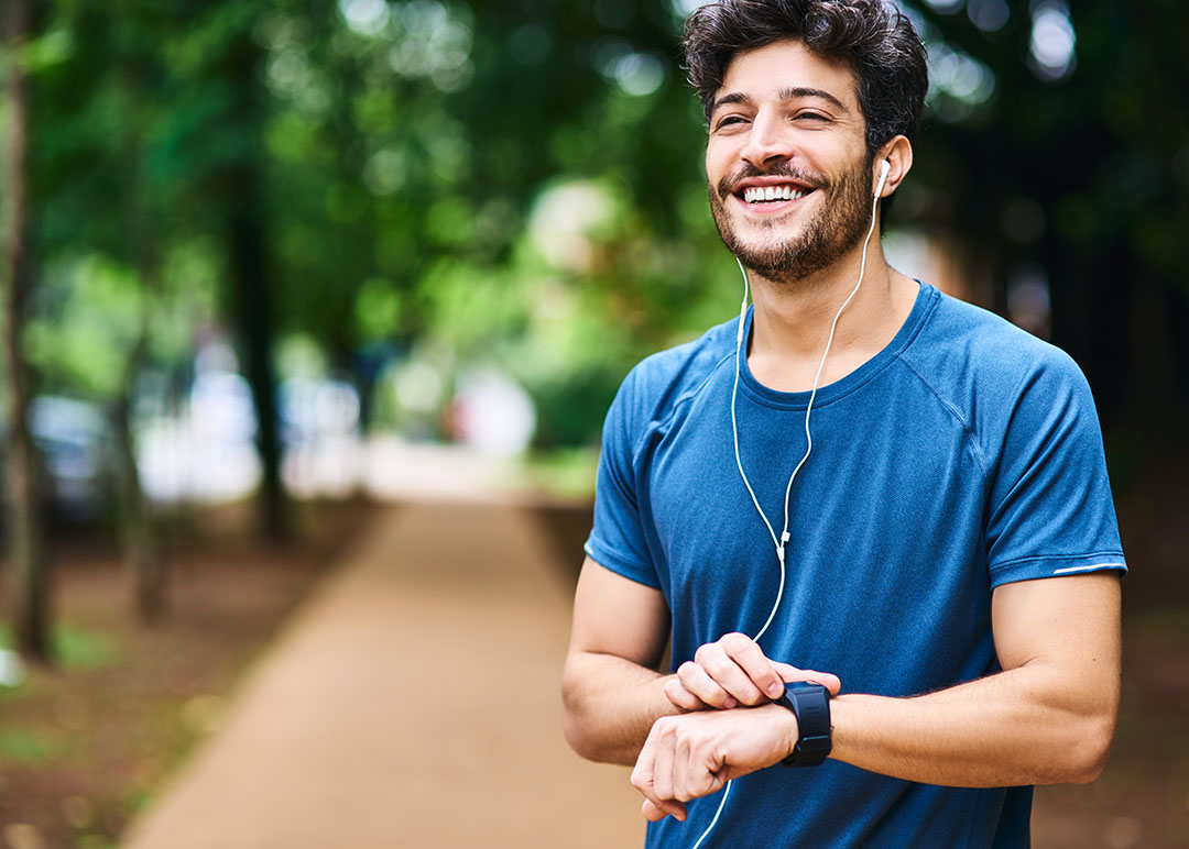 A young man checking his watch while exercising outdoors with earbuds in.
