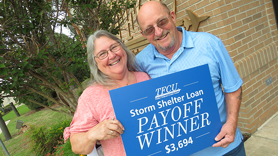 Older man and woman holding a Storm Shelter Payoff Winner sign.
