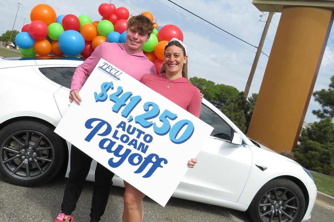 A mother and son holding a sign in front of a car