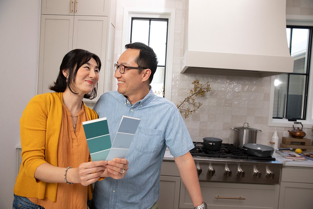 An older couple looking at each other in a kitchen while holding color swatches
