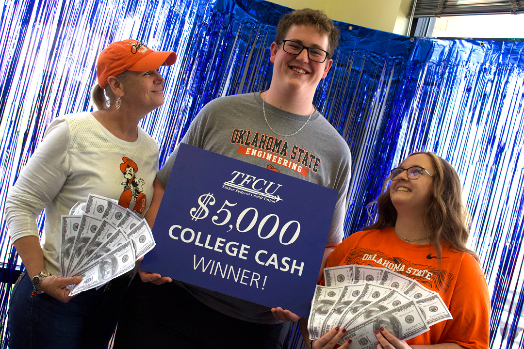 Young man who is a student is standing with two family members while holding up a sign that says $5,000 college cash winner
