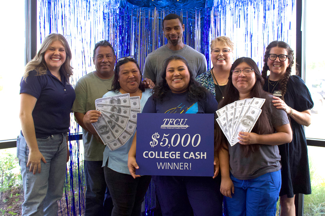 Young woman who is a student is standing with her family of 7 while holding up a sign that says $5,000 college cash winner