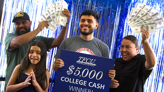 Young man who is a student is standing with her family of 3 while holding up a sign that says $5,000 college cash winner
