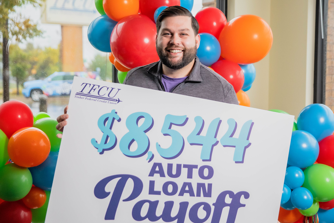 Man standing in front of colorful balloons, smiling and holding a sign that says $8,544 Auto Loan Payoff.