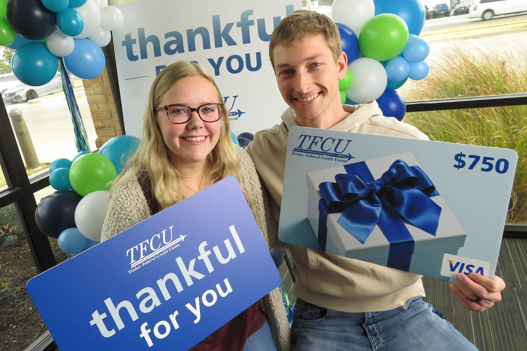 A young couple looking at the camera and holding up two signs with a thankful for you sign behind them