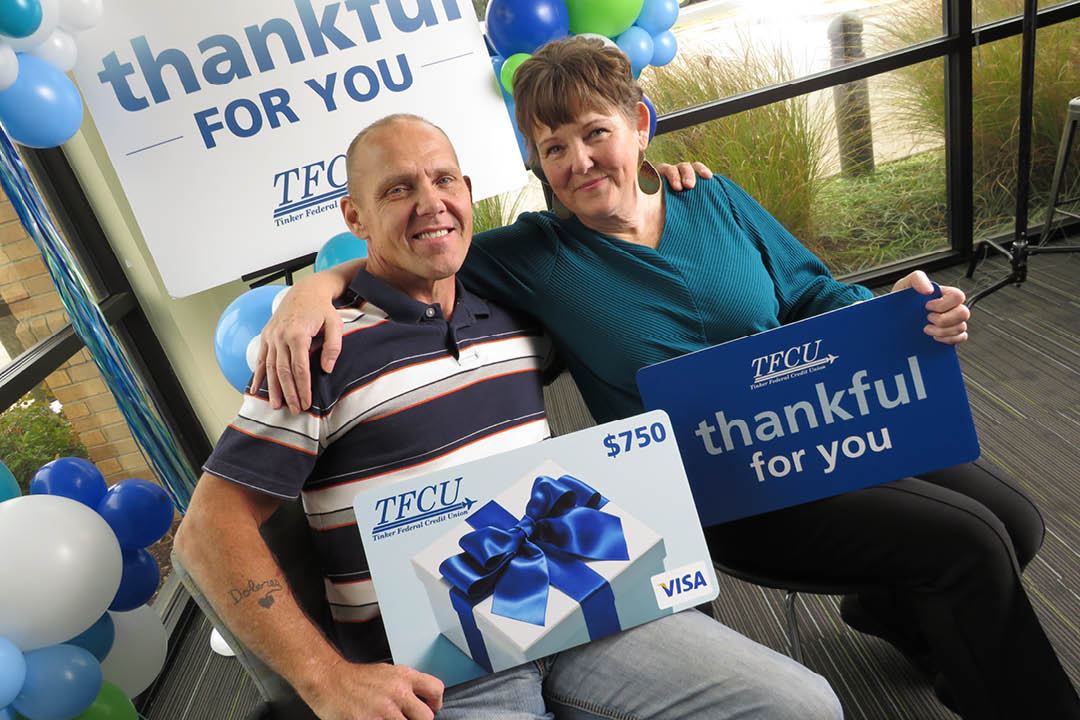 An older couple embracing each other while looking at the camera and each are holding up a sign.